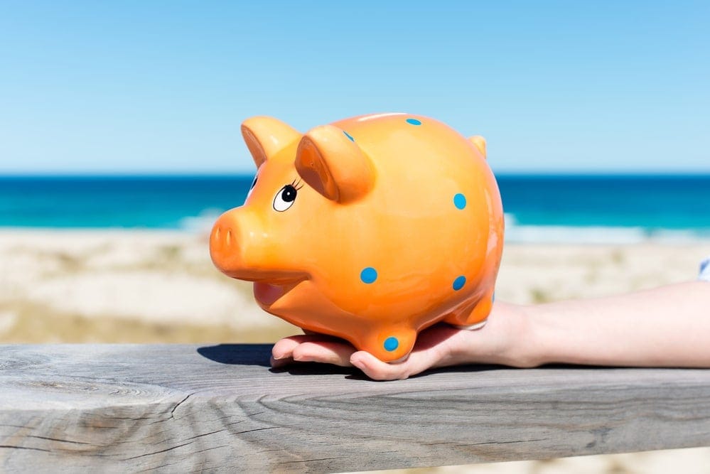 woman´s hand holding piggy bank by the beach